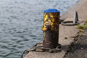 Small harbor architecture details in Helsinki, Finland, June 2019. Old rusty metal pole to which you can chain a boat. Also some concrete floor and calm sea are in the photo. Color image.
