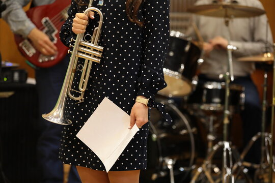 A woman musician with a musical instrument trumpet and a white sheet stands on stage in front of a jazz band