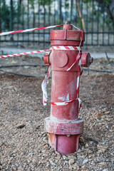 Red fire hydrant standing in the middle of gravel in front of a fence. Barrier tape is wrapped...