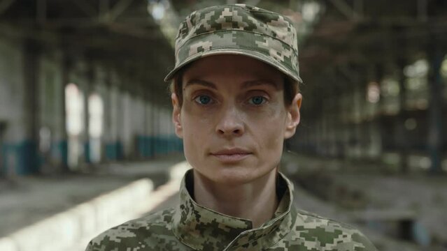 Close up of confident female officer with fatigue in eyes looking at camera while standing at factory after fight. War, military, army and people concept.