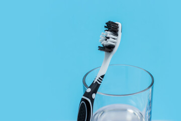 A black and white toothbrush and glass of mouthwash on blue background with copy space.