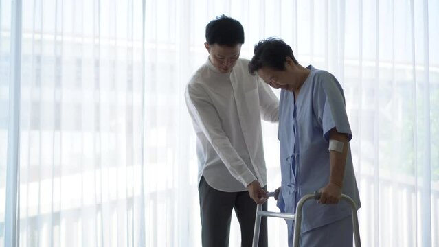 Adult Asian son help mother do physical therapy using walker in hospital love encourage and care family