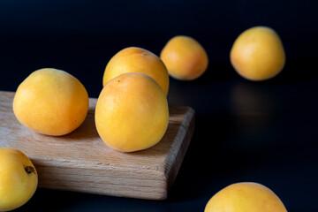 Ripe apricots on a wooden board and next to it. Dark key. Selective focus.