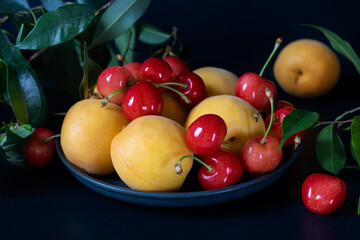 Ripe cherries with leaves and apricots on a round platter.
