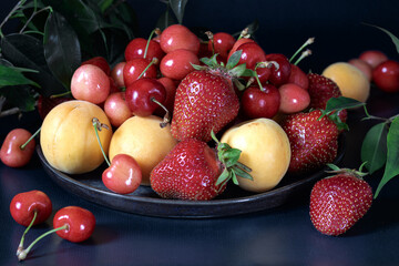 Cherries, apricots and strawberries on a round platter. Leaves in the background.