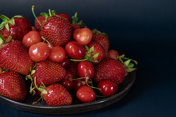 Strawberries and cherries on a round dish. Close-up. Dark key.