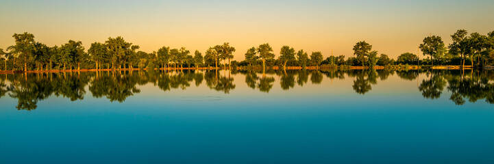 Tranquil water reflections of the cottonwood trees at Deshler Reservoir Park in Ohio