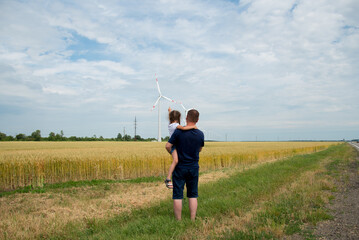 A girl and her dad look at the wind generator in the field. Ecology. Future.