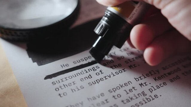 Hand using black marker to censor text on sensitive secret document or memo. Black lines are drawn on classified paper before it is declassified. Erasing information or hiding cover-up or involvement