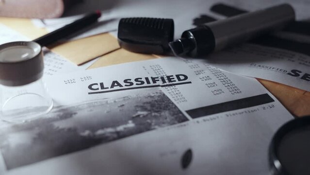 Slow push in on classified document with stamp next to secret material on a desk. Camera moves slowly on close up showing sensitive memo next to envelopes and folders on dark office desk