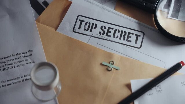 Slow pan across different top secret classified documents laid on office desk. Papers inside manila envelopes and folder with sensitive information. Leaked or uncovered memos by military or government