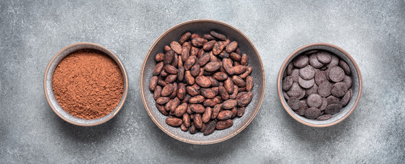 Cocoa beans, cocoa powder and chocolate in a bowl, grunge gray background. Top view, banner.