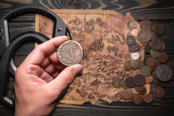 Ancient coin in treasure hunter hand close up on the metal detector, ancient coins and old treasure map background. Treasure hunting concept.