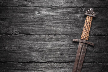 Old battle sword on the black wooden table background top view.