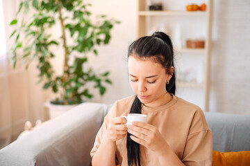 A happy young woman drinks a cup of tea on an autumn morning. A dreamy girl is sitting in the living room with a cup of hot coffee. A beautiful woman at home.