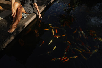 Fototapeta na wymiar Girl feeds the fish by hand in a small pond in the yard. Koi fish, popular recreational or good luck pets, feng shui beliefs meaning good luck.