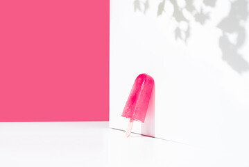 Paleta de hielo con sabor a frambuesa apoyada contra una pared blanca. Palo de helado rosa. Espacio...