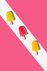 Paletas de hielo de colores. Palitos de helado naranja, rojo y amarillo sobre fondo rosa. Concepto...