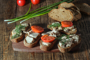 Cooked sandwiches with cod liver, tomatoes and herbs on a wooden background, a quick and healthy breakfast