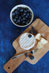 Ceramic bowl with fresh garden blueberry, creamy cheese on wooden board. Simple composition still life with summer food. 