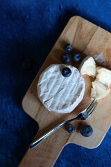 Still life with Brie cheese, blueberry and wooden board. Blue textured background with copy space. 