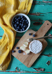 Ceramic bowl with fresh garden blueberry, creamy cheese on wooden board. Simple composition still life with summer food. 