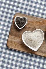 large bowl of raw white rice and a small long black rice on a wooden board top view
