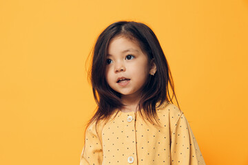 a beautiful, happy, fashionably dressed little girl stands on an orange background and looks away....