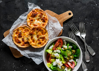 Delicious lunch table - mini canned tuna, mozzarella quiche and fresh Greek salad on a dark background, top view