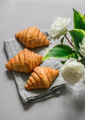 Homemade fresh croissants and a bouquet of peonies on a gray background, top view