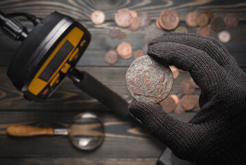 Treasure seeker hold in hand an ancient coin close up on the metal detector on the table background.