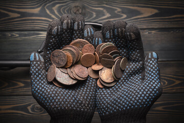 Hand full of old coins and recreational metal detecor. Treasure hunting concept background.