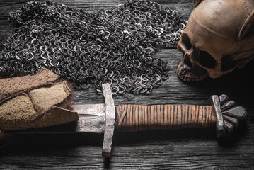 Ancient sword wrapped in the beast skin and chain mail armor on the table close up.