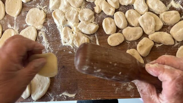 grandmother prepares delicious dumplings or pies or dumplings for her grandson she shakes dough, cuts it into pieces and sculpts on the table there are circles of dough she is sprinkled with flour