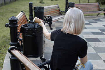  a woman throws a glass of coffee into the trash can while sitting on a bench