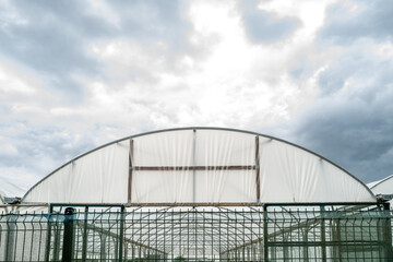  Shallow focus of the front of a large, industrial poly tunnel showing the supporting beams and part of its interior. Seen against looming storm clouds.