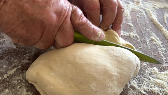 grandmother prepares delicious dumplings or pies or dumplings for her grandson she shakes dough, cuts it into pieces and sculpts on the table there are circles of dough she is sprinkled with flour