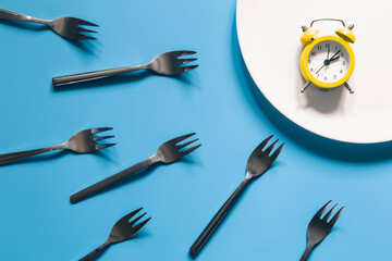 Alarm clock on a white plate with forks on blue background.