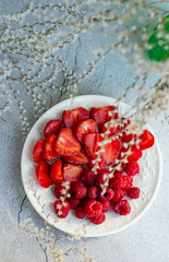 sliced ripe red strawberries in a white plate on a light gray background