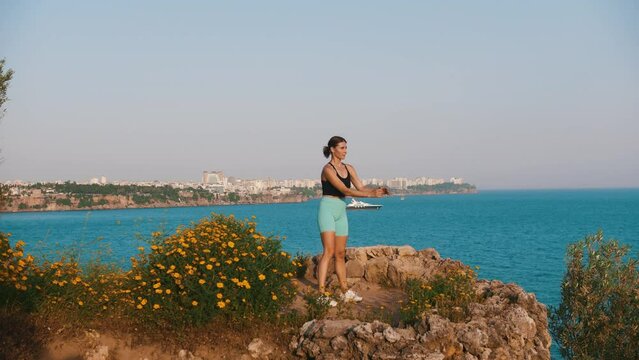 Sportive woman working out on the hill by the sea - squatting on the spot