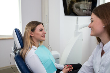 Fototapeta premium She is sitting in the dentist's chair. The dentist explains and advises the patient.
