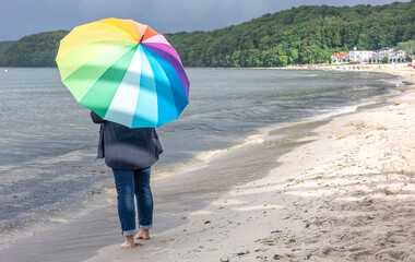 A woman with a rainbow umbrella on the seashore.