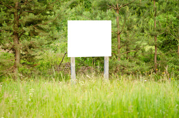 A white empty billboard in the forest among the trees. Posting information in a public park or drawing attention to environmental issues. Summer, copy space.