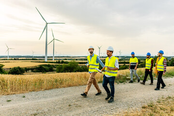 Group of technicians and engineers people walking on a field path at a wind farm - Renewable and...