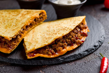 Quesadilla with beef, cheese, bbq sauce and sauces on dark stone plate macro close up