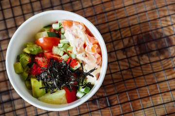 avocado, rice, cucumber, tomato and salmon poke on a wooden background. Asian dish copy space