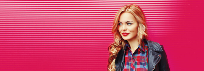Portrait of beautiful blonde young woman with red lipstick wearing black rock jacket on pink...