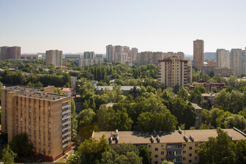 Fototapeta premium The urban landscape is the city of Reutov with residential buildings among the lush green foliage of trees and a clear blue sky on a summer day and a space for copying