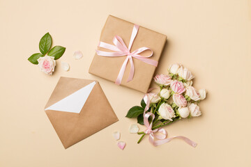 Envelope, gift box and rose flowers on color background, top view