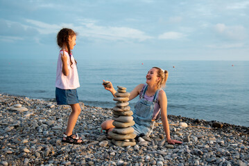 A mother and daughter 6 years old on the beach build a castle of stones. They socialize and have fun together. Family. Summer. Vacation.
